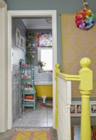 Vue depuis le palier jusqu'à la salle de bains colorée avec baignoire autoportante jaune, carreaux de métro blancs et murs gris.