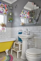 Salle de bain colorée avec une baignoire autoportante jaune, des carreaux de métro blancs et un miroir en forme d'éventail.
