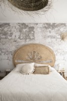 Mur de plâtre nu derrière le lit avec tête de lit en rotin