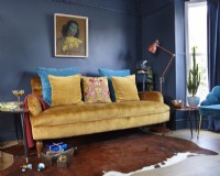 Salon avec canapé jaune moutarde, imprimé 'The Green Lady', mur peint en bleu marine, tables d'appoint rétro et cadeaux de Noël.