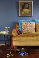 Détail du salon avec un canapé jaune moutarde, un imprimé 'The Green Lady', un mur peint en bleu marine et des tables d'appoint rétro avec des cadeaux de Noël.