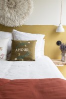 Coussin brodé sur lit avec demi-mur peint moutarde derrière