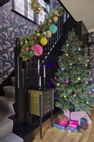 Couloir de Noël avec un sapin décoré et des cadeaux. Rampe peinte en noir et papier peint montant l'escalier.