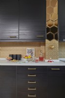 Détail de la cuisine montrant des armoires marron foncé, des carreaux de miroir dorés et du papier peint texturé peint en or.
