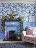 Détail du salon montrant une cheminée décorée pour Noël, un papier peint imprimé jungle et des boiseries bleues.
