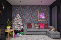 Salon ouvert décoré pour Noël. Canapé confortable avec coussins colorés, papier peint à motifs, murs noirs et poêle à bois.