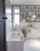 Salle de bain avec papier peint à motifs, miroir rond et robinetterie dorée.
