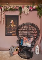 Détail de la chambre montrant une chaise paon noire, des décorations florales et des œuvres d'art sur les murs peints en rose.