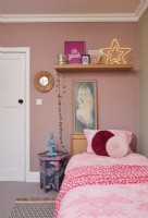 Chambre avec des murs roses, une table d'appoint tapissée et des œuvres d'art rétro.