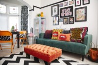 Salon coloré avec canapé vert, repose-pieds orange et mur de galerie.