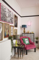 Détail coloré du salon avec un fauteuil rose, des tables gigognes et un mur de galerie.