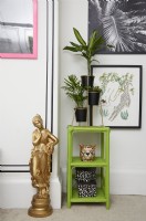 Détail de la chambre avec un effet de faux lambris noir (avec du ruban washi noir), des œuvres d'art encadrées, des étagères vertes avec des plantes et une statue dorée.