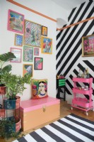 Détail coloré du bureau à domicile avec des illustrations encadrées, un mur à rayures en vinyle noir et un chariot à boissons fluorescent.
