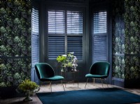 Salon avec papier peint à motifs, fauteuils verts et volets