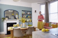 Cuisine-salle à manger ouverte avec des murs bleus, une cheminée victorienne et des sièges près de la fenêtre.