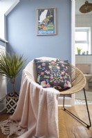 Détail de la chambre montrant une chaise en osier, des œuvres d'art sur des murs peints en bleu.