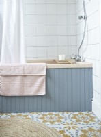 Détail de la salle de bain montrant une baignoire à panneaux bleus et un sol au look rétro.
