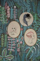 Détail du salon montrant des broderies encadrées de visages de femmes avec du papier peint à motifs.