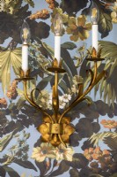 Applique d'éclairage en forme de feuille d'or sur le mur avec du papier peint à motifs floraux.