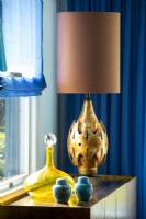 Lampe de couleur bronze sur table avec carafe en verre jaune et pots en céramique bleue.
