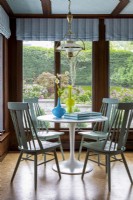 Table à manger ronde sur pied blanc avec chaises en bois et vue sur le jardin.