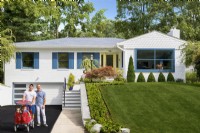 Maison familiale blanche en briques modernes du milieu du siècle à un étage avec volets bleus et pelouse verte.