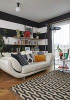 Murs à rayures noires et blanches dans un salon moderne à aire ouverte. Avec un canapé en cuir crème et un tapis à motifs.