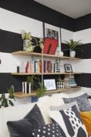 Détail d'étagères ouvertes dans un salon moderne à plan ouvert avec des murs à rayures noires et blanches. Avec des pots de plantes en béton peints à la main.