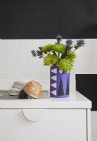 Détail de la cuisine montrant un vase en béton violet, des carreaux hexagonaux et des murs peints à rayures noires et blanches.