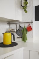 Détail de la cuisine contemporaine montrant une bouilloire jaune, des ustensiles suspendus et des carreaux hexagonaux blancs.