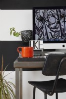 Espace bureau à domicile dans un espace de vie à aire ouverte. Avec des murs rayés noirs et blancs, un tabouret et des plantes.