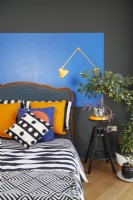 Formes bauhaus peintes audacieuses et colorées dans une chambre contemporaine. Avec une tête de lit antique, des tissus d'ameublement à motifs et une lampe anglepoise jaune.