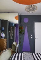 Formes bauhaus peintes audacieuses et colorées dans une chambre contemporaine. Montrant des formes peintes en violet et orange avec une literie à rayures monochromes.