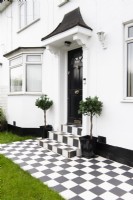 Pavage à carreaux noir et blanc et marches menant à une porte d'entrée noire dans une maison blanche