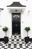 Pavage à carreaux noir et blanc et marches menant à une porte d'entrée noire dans une maison blanche