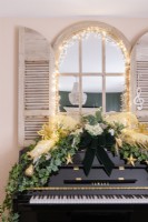 Piano droit noir décoré de lierre, de plumes et de boules de Noël avec un miroir à obturateur derrière