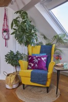 Détail du salon mansardé montrant un fauteuil jaune de style milieu du siècle, une table basse et des plantes.