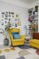 Coin salon montrant un fauteuil et un repose-pieds jaunes de style milieu du siècle avec un mur de galerie, une étagère et des plantes.
