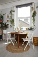 Salon multifonctionnel avec table à manger à abattant. Plantes suspendues et œuvres d'art sur les murs.
