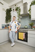 Femme dans une cuisine avec des carreaux de métro bleus, des plantes suspendues et une casserole verte.