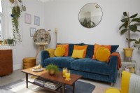 Salon avec canapé bleu canard, coussins orange et jaune et une table basse rétro.