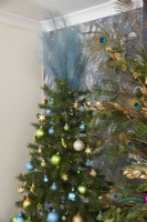 Détail du salon de Noël montrant un arbre décoré de guirlandes lumineuses, de boules et de plumes de paon.
