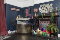 Salon avec un bar à boissons doré, des murs peints en bleu foncé et une cheminée décorée.