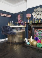 Salon avec un bar à boissons doré, des murs peints en bleu foncé et une cheminée décorée.