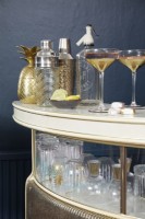 Salon montrant le détail du bar à boissons doré, avec des verres à cocktail et un shaker.