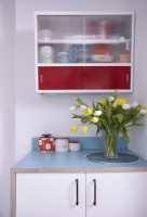 Détail de cuisine en contreplaqué montrant des plans de travail bleus et une armoire murale rétro rouge.