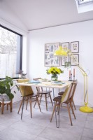 Salle à manger ouverte avec des chaises vintage Ercol et un lampadaire jaune.