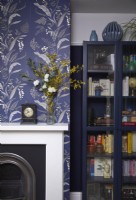 Détail de la salle à manger montrant une cheminée avec du papier peint à motifs et un meuble de rangement bleu foncé.