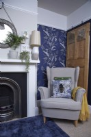 Salon avec cheminée, fauteuil cosy et papier peint à motifs bleus.