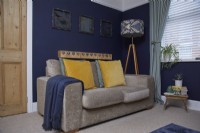 Salon avec des murs peints en bleu foncé, un canapé en velours gris et un lampadaire à motifs.